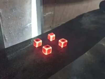 Burning cube charcoal briquettes glowing red-hot on a metal mesh tray during a quality control test.