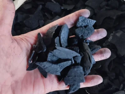 Premium quality raw coconut shell charcoal pieces held by hand, suitable for briquette production.